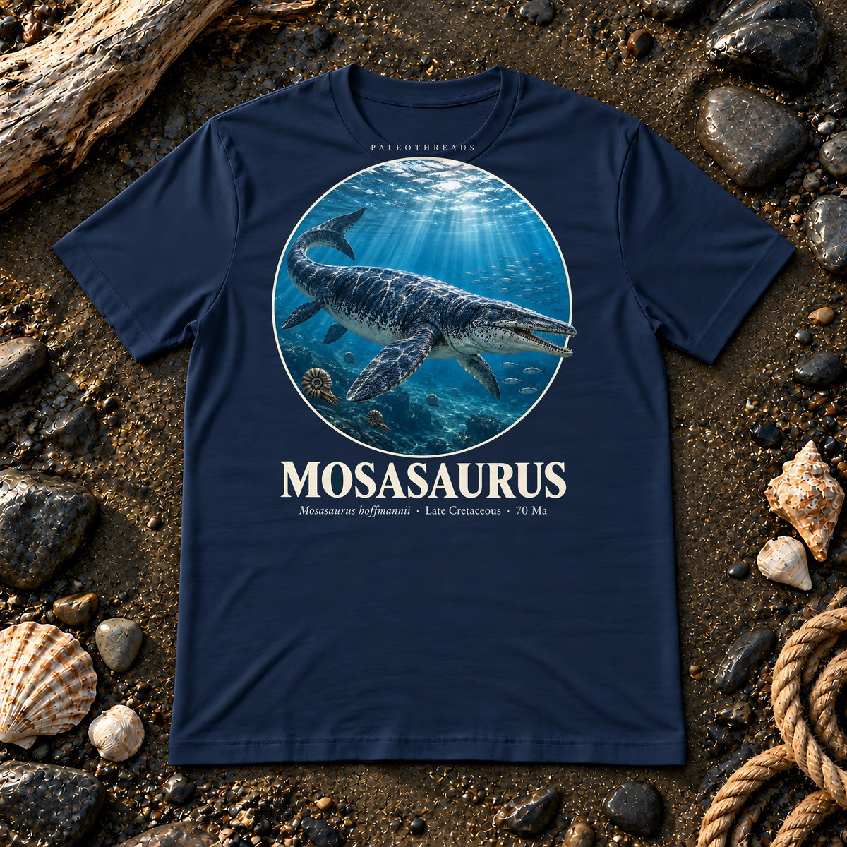 Mosasaurus t-shirt flat lay – navy PaleoThreads paleo art tee on a fossil beach with driftwood