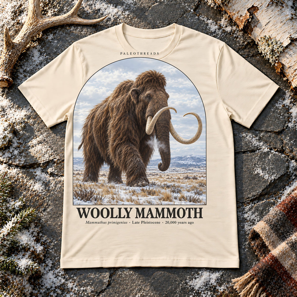 Woolly Mammoth t-shirt flat lay – natural PaleoThreads paleo art tee on frosty slate with an antler