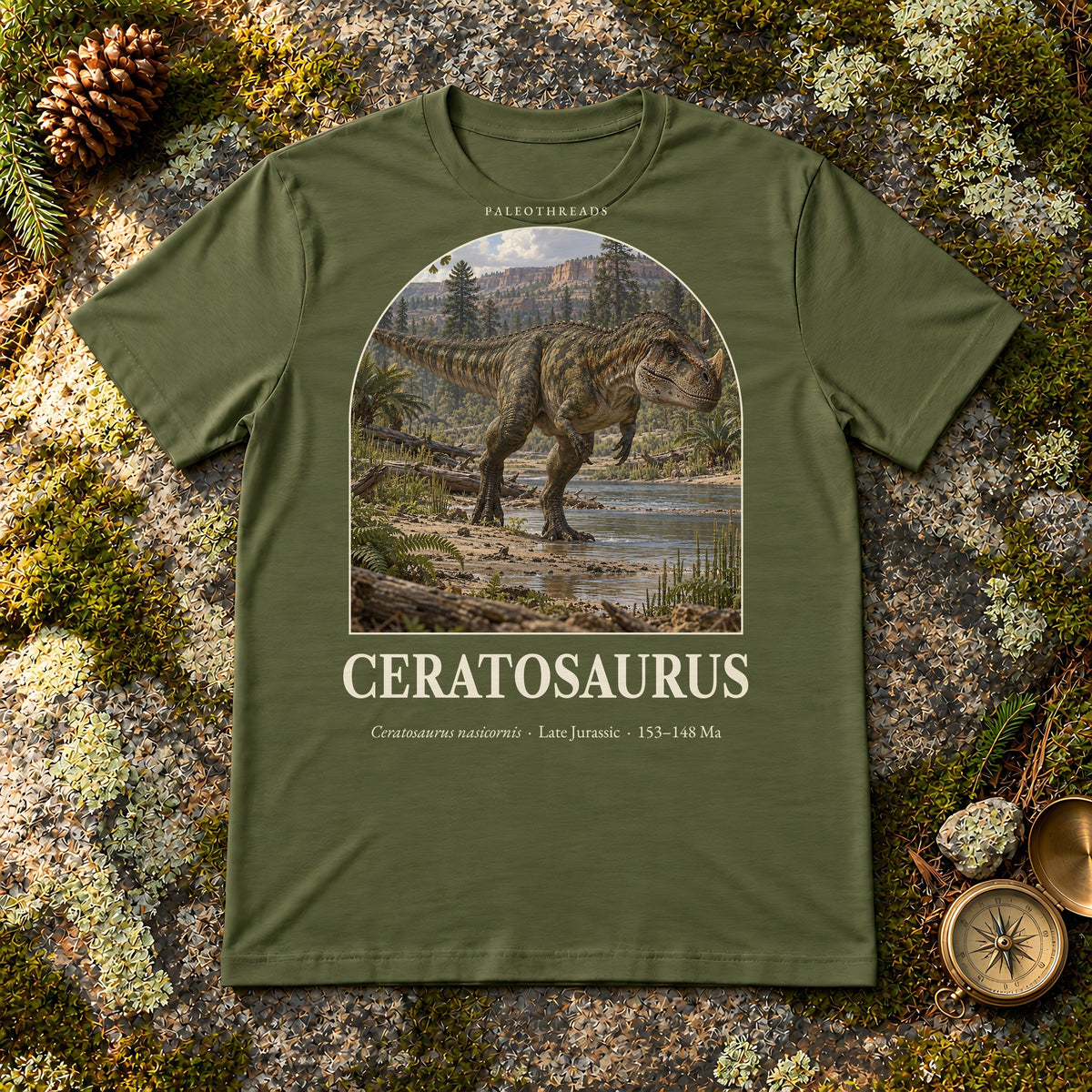 Ceratosaurus t-shirt flat lay – military green PaleoThreads paleo art tee on mossy rock with a brass compass