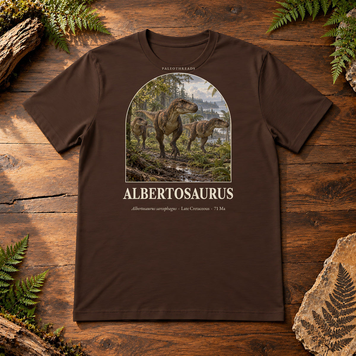 Albertosaurus t-shirt flat lay – brown PaleoThreads paleo art tee on a walnut field desk with ferns