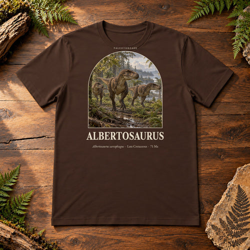 Albertosaurus t-shirt flat lay – brown PaleoThreads paleo art tee on a walnut field desk with ferns