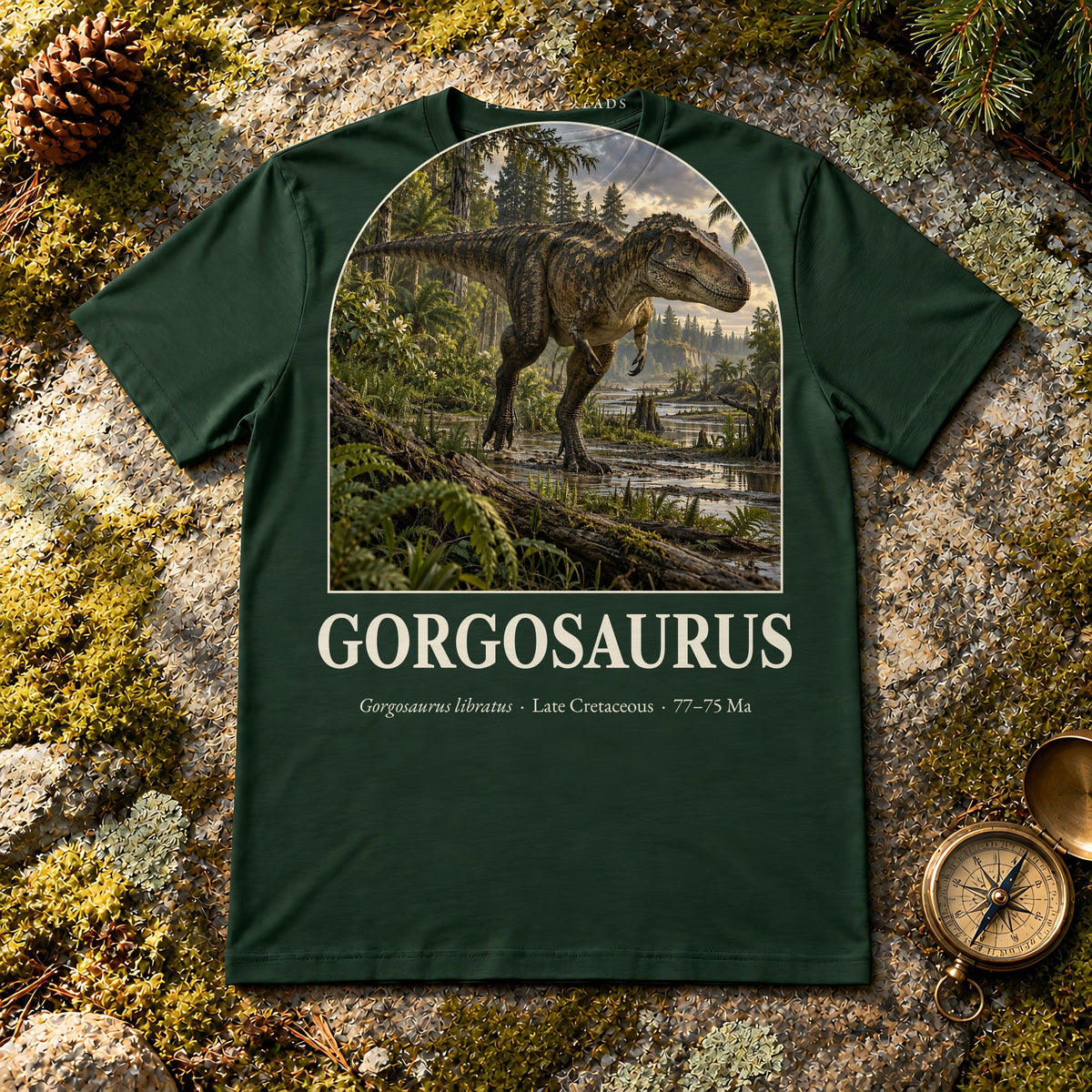 Gorgosaurus t-shirt flat lay – forest PaleoThreads paleo art tee on mossy rock with a brass compass