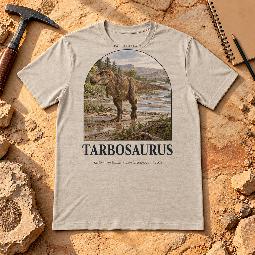 Tarbosaurus t-shirt flat lay – heather dust PaleoThreads paleo art tee on sandstone with a rock hammer