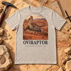 Oviraptor t-shirt flat lay – heather dust PaleoThreads paleo art tee on sandstone with a rock hammer