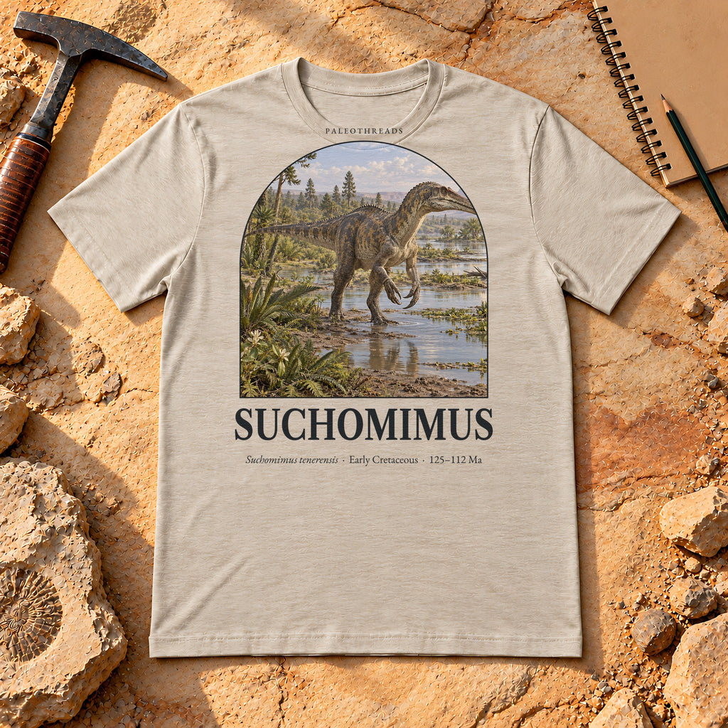 Suchomimus t-shirt flat lay – heather dust PaleoThreads paleo art tee on sandstone with a rock hammer