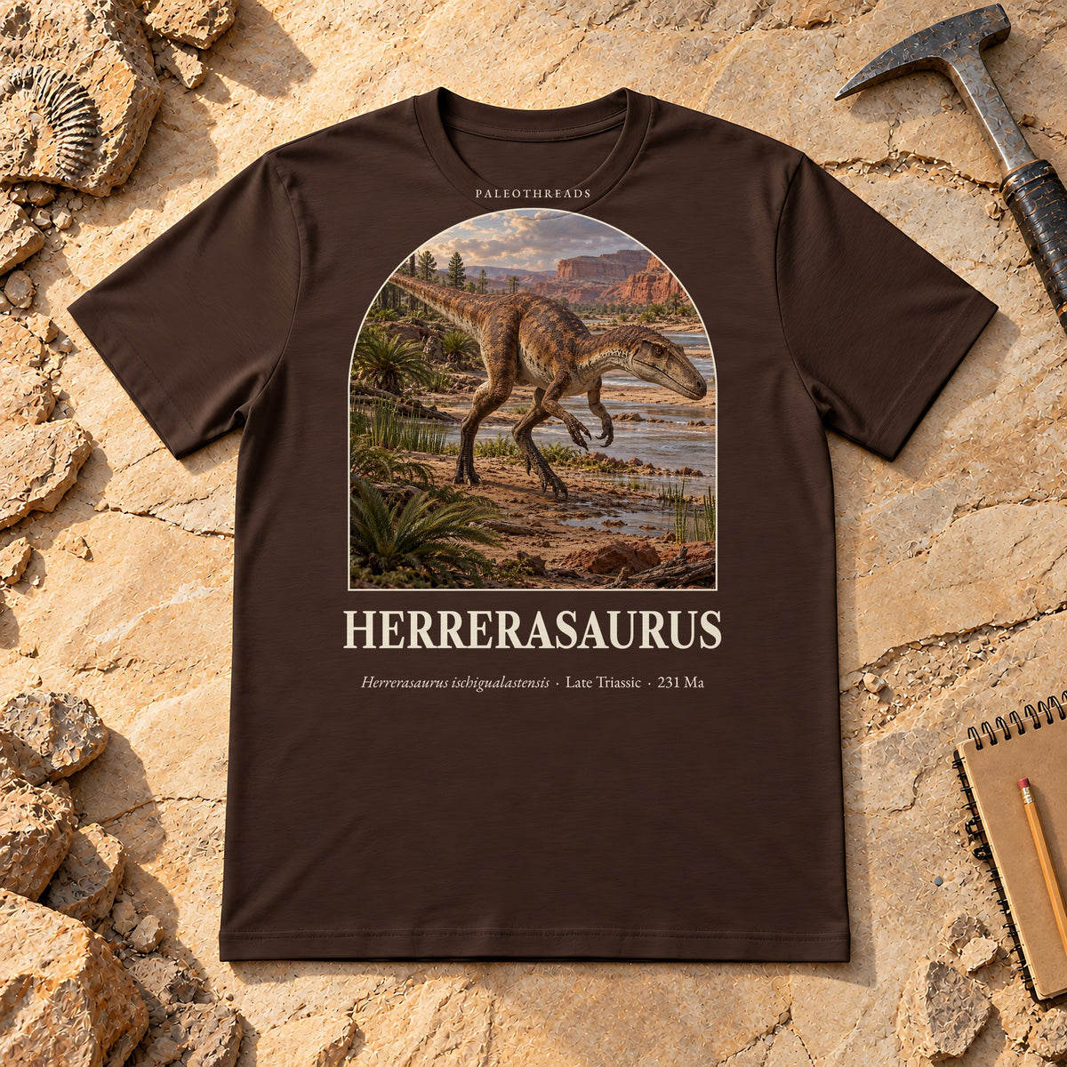Herrerasaurus t-shirt flat lay – brown PaleoThreads paleo art tee on sandstone with a rock hammer