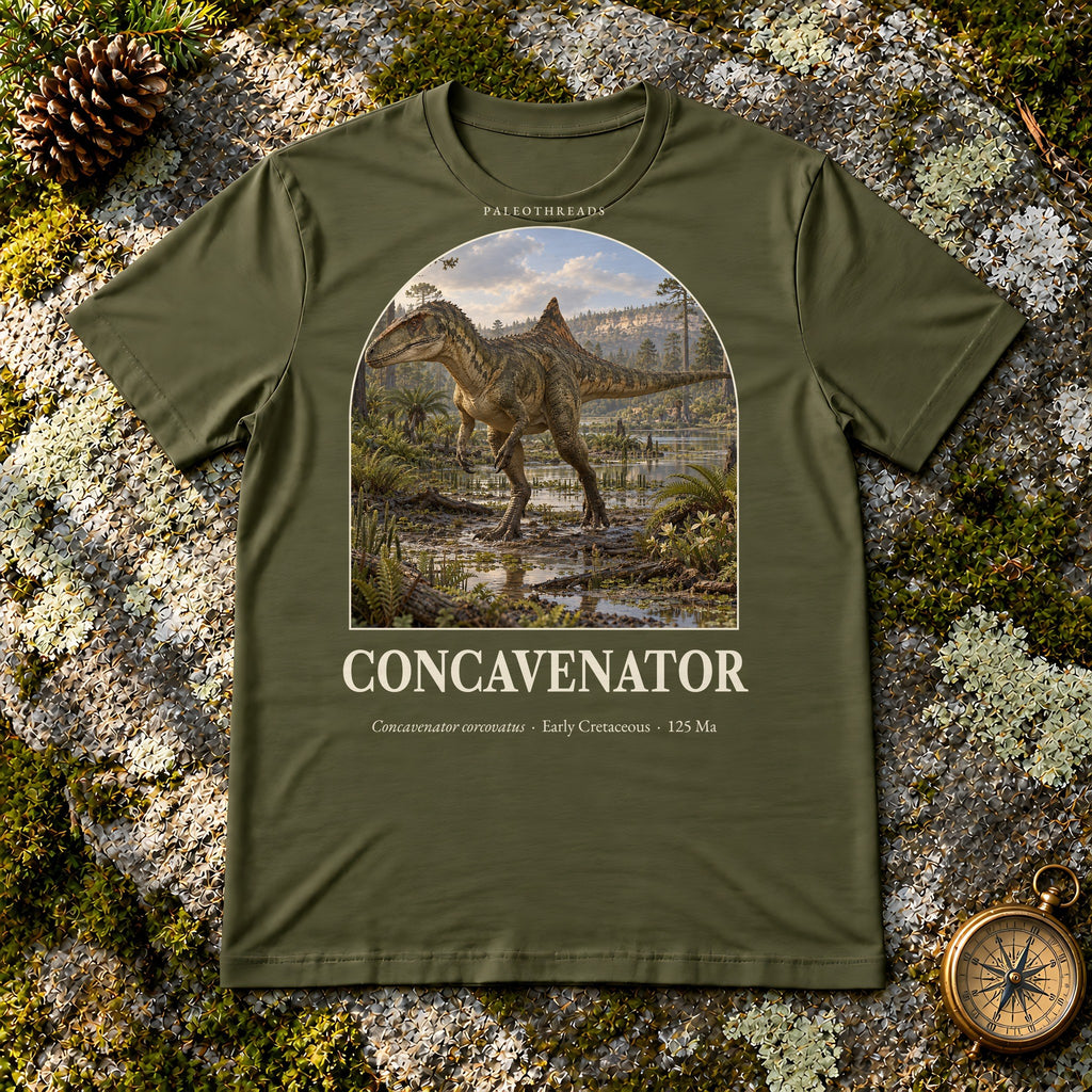 Concavenator t-shirt flat lay – olive PaleoThreads paleo art tee on mossy rock with a brass compass