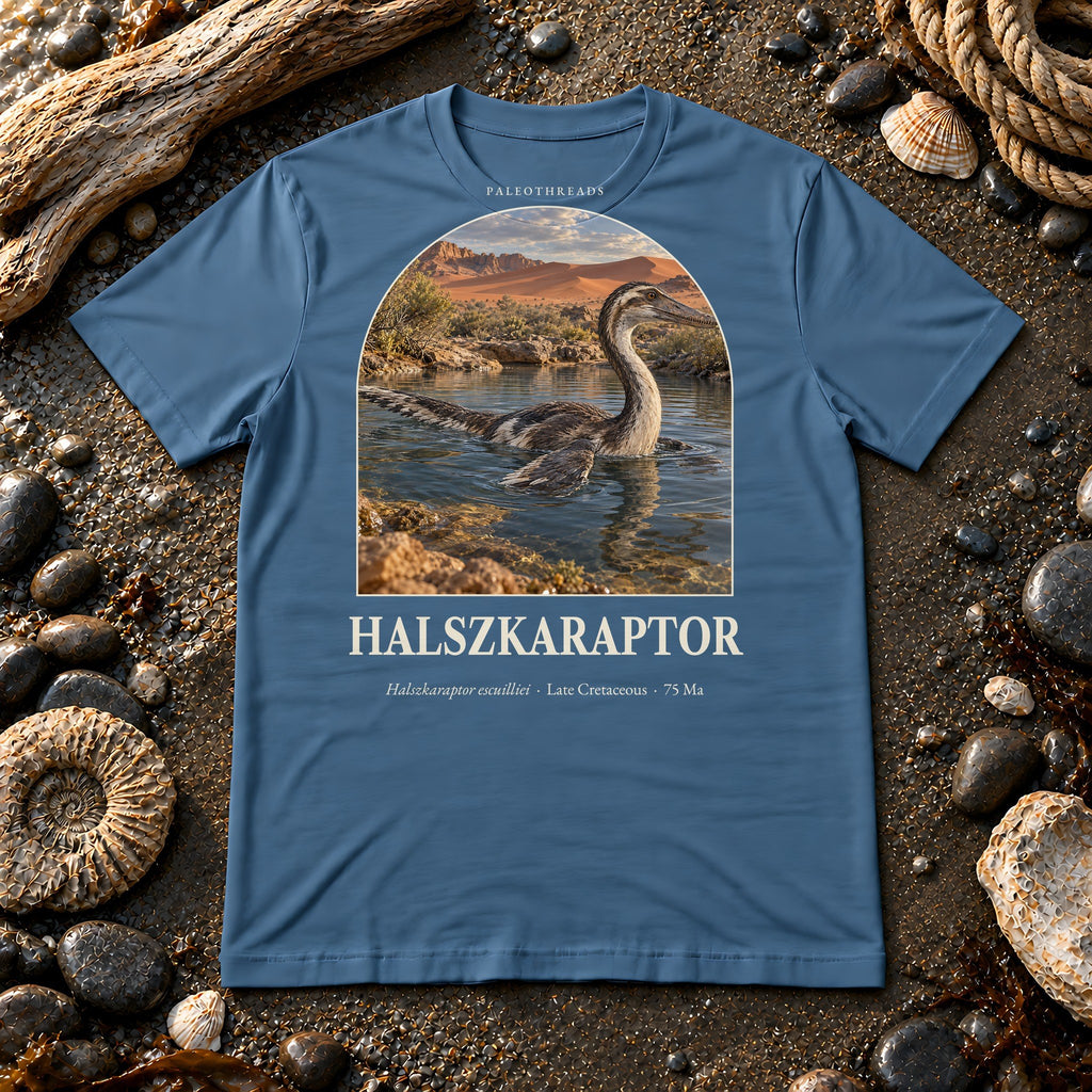 Halszkaraptor t-shirt flat lay – steel blue PaleoThreads paleo art tee on a fossil beach with driftwood