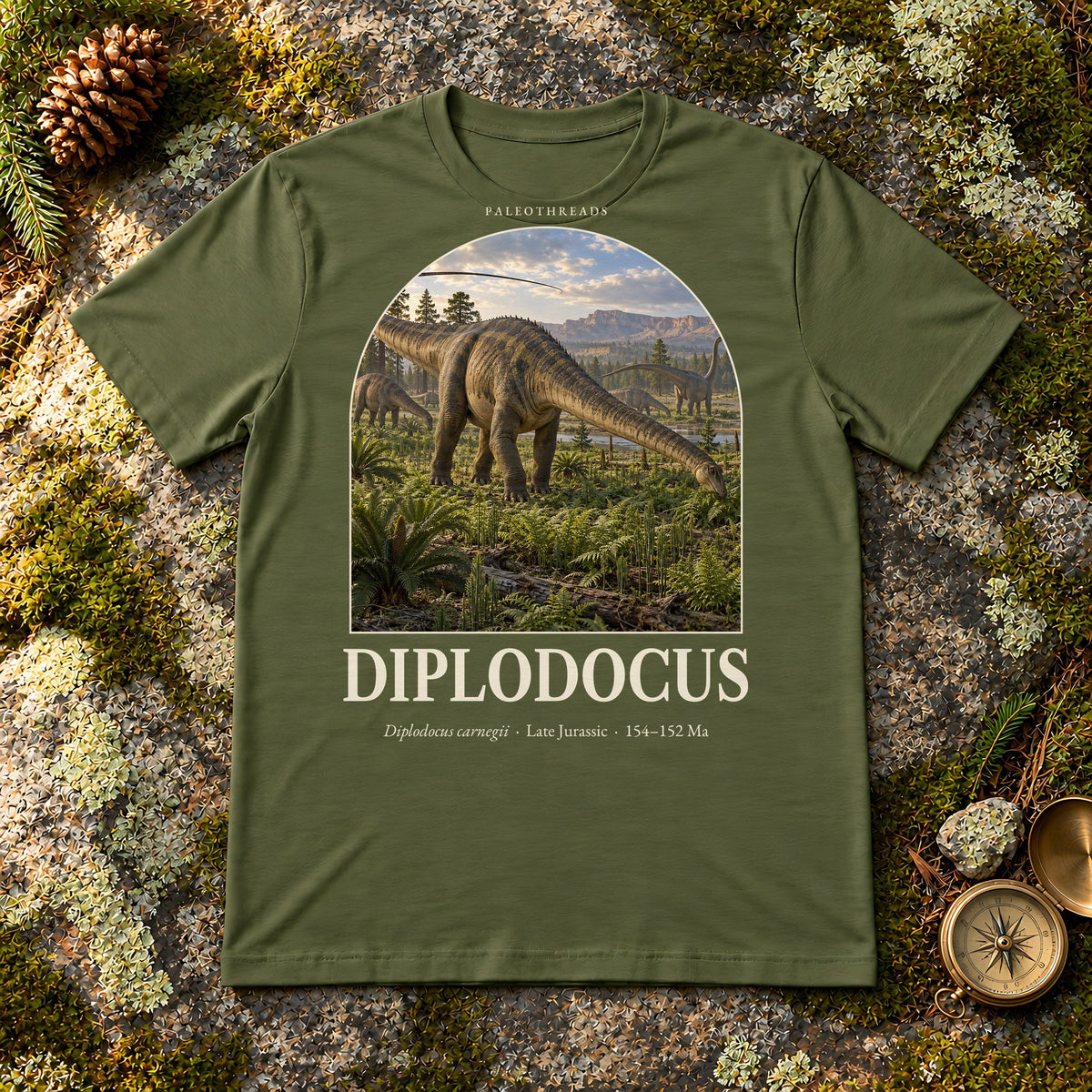 Diplodocus t-shirt flat lay – military green PaleoThreads paleo art tee on mossy rock with a brass compass