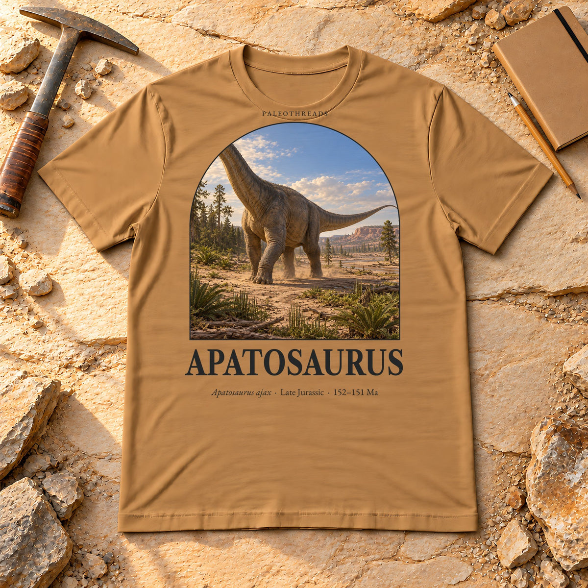 Apatosaurus t-shirt flat lay – toast PaleoThreads paleo art tee on sandstone with a rock hammer