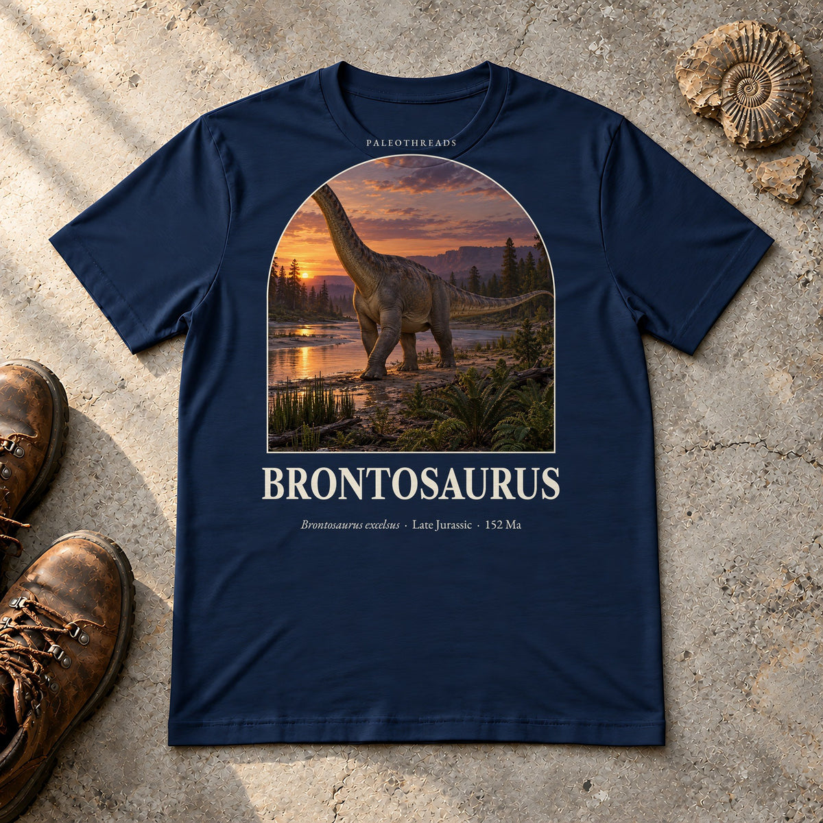 Brontosaurus t-shirt flat lay – navy PaleoThreads paleo art tee with hiking boots and an ammonite