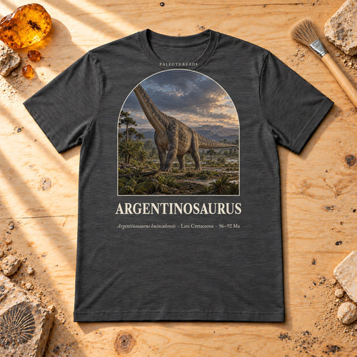 Argentinosaurus t-shirt flat lay – dark grey heather PaleoThreads paleo art tee on a fossil prep bench with amber