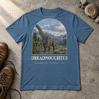 Dreadnoughtus t-shirt flat lay – steel blue PaleoThreads paleo art tee with hiking boots and an ammonite