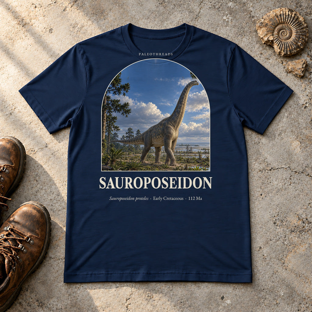 Sauroposeidon t-shirt flat lay – navy PaleoThreads paleo art tee with hiking boots and an ammonite