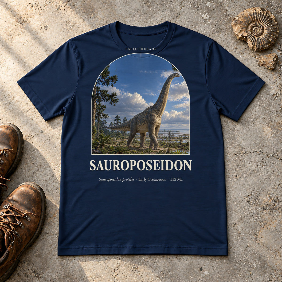 Sauroposeidon t-shirt flat lay – navy PaleoThreads paleo art tee with hiking boots and an ammonite