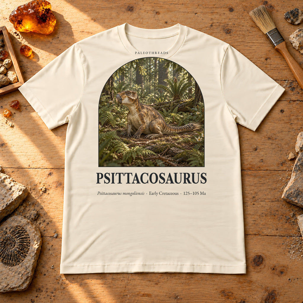 Psittacosaurus t-shirt flat lay – soft cream PaleoThreads paleo art tee on a fossil prep bench with amber