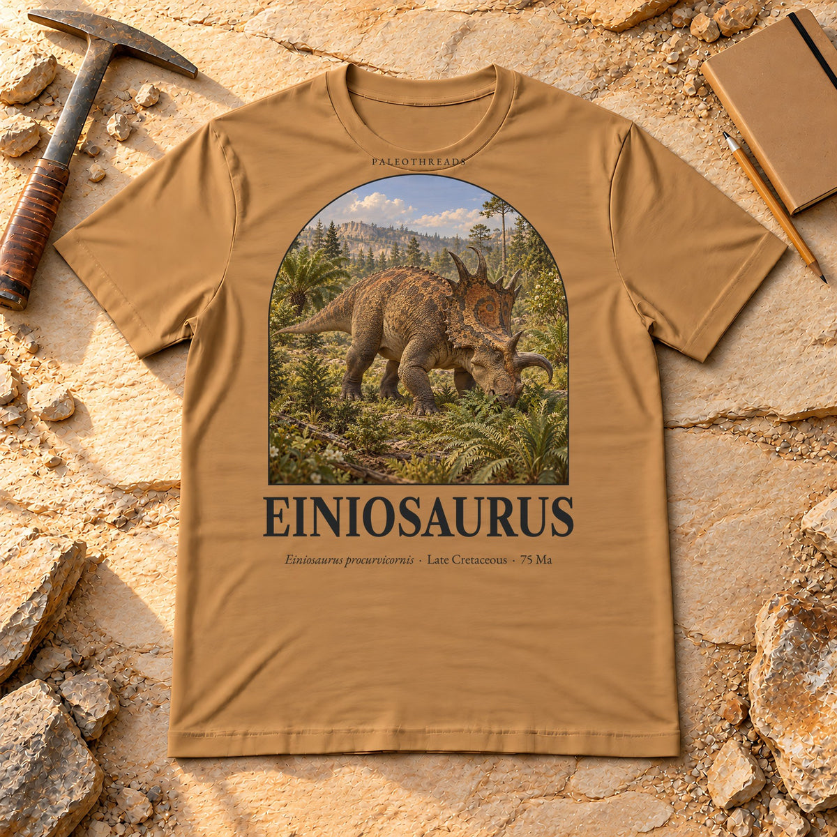 Einiosaurus t-shirt flat lay – toast PaleoThreads paleo art tee on sandstone with a rock hammer