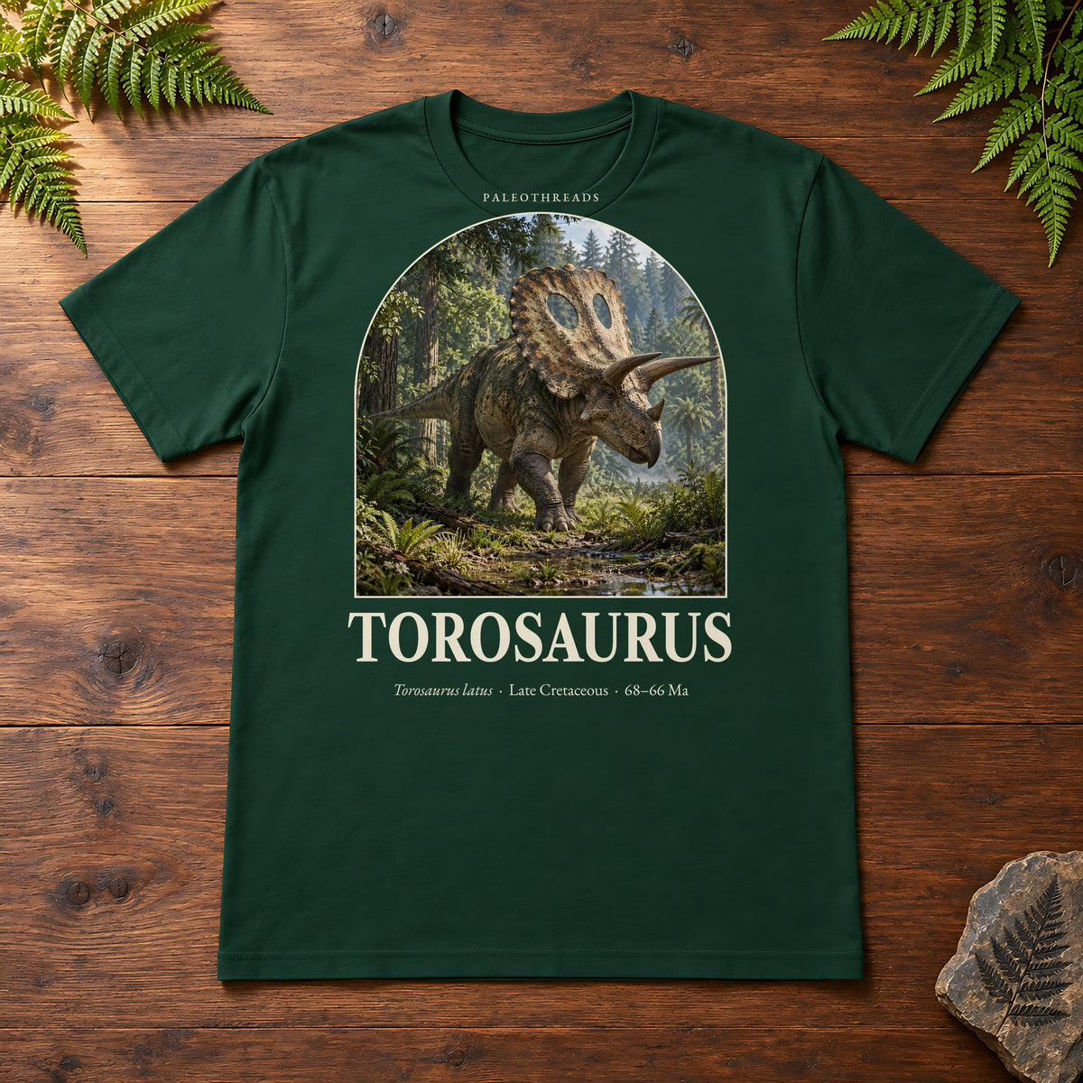 Torosaurus t-shirt flat lay – forest PaleoThreads paleo art tee on a walnut field desk with ferns