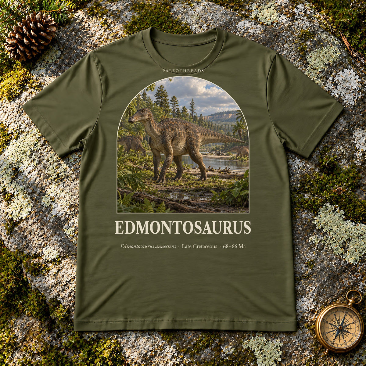 Edmontosaurus t-shirt flat lay – olive PaleoThreads paleo art tee on mossy rock with a brass compass