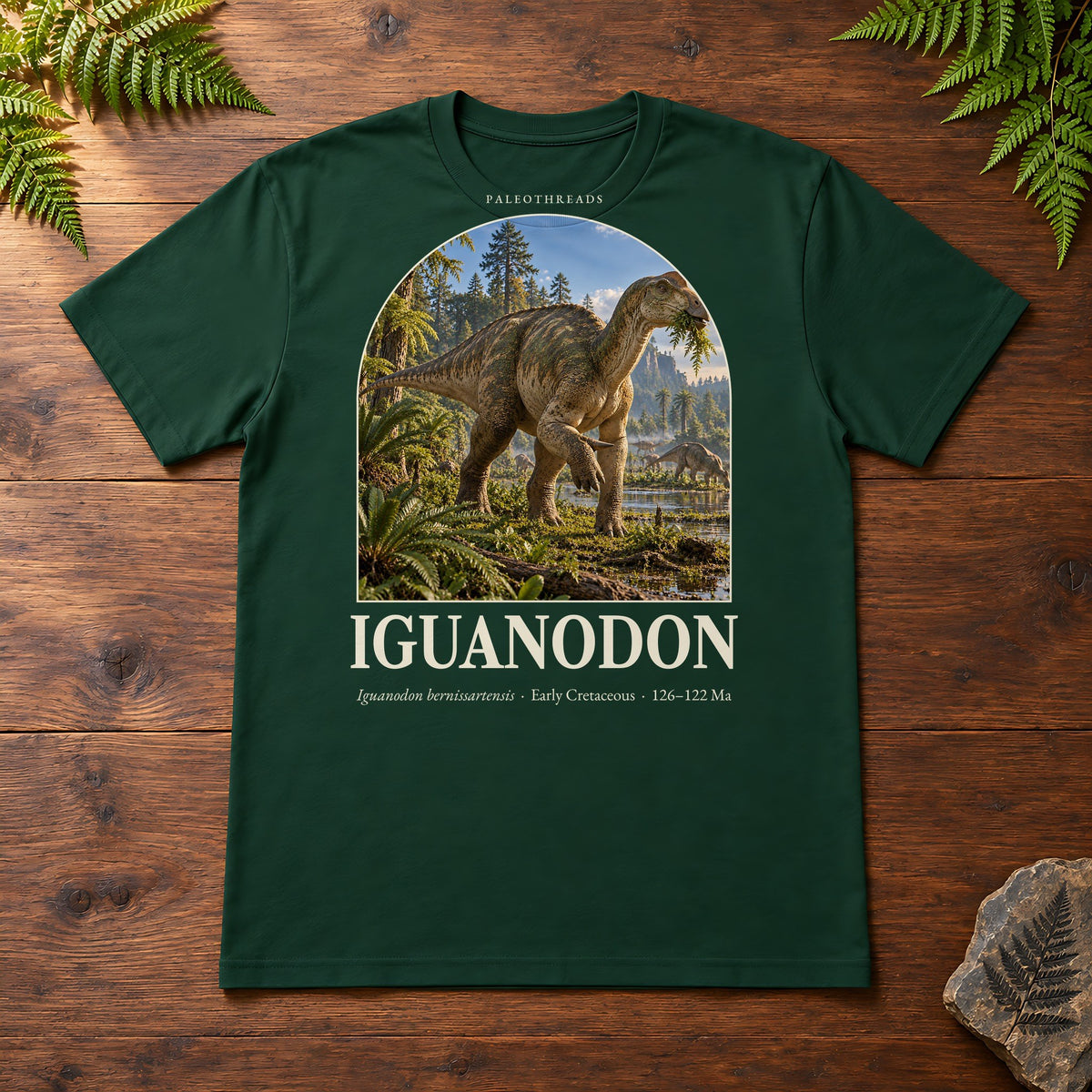 Iguanodon t-shirt flat lay – forest PaleoThreads paleo art tee on a walnut field desk with ferns