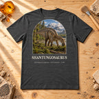 Shantungosaurus t-shirt flat lay – dark grey heather PaleoThreads paleo art tee on a fossil prep bench with amber