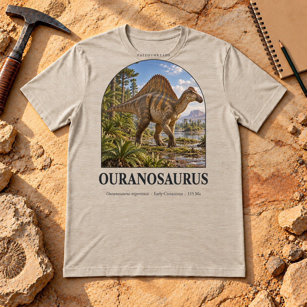 Ouranosaurus t-shirt flat lay – heather dust PaleoThreads paleo art tee on sandstone with a rock hammer