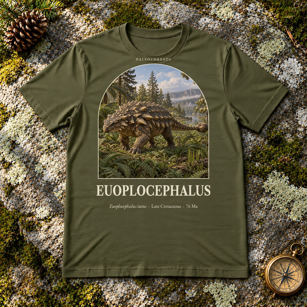 Euoplocephalus t-shirt flat lay – olive PaleoThreads paleo art tee on mossy rock with a brass compass