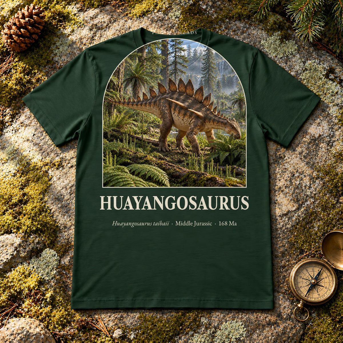 Huayangosaurus t-shirt flat lay – forest PaleoThreads paleo art tee on mossy rock with a brass compass