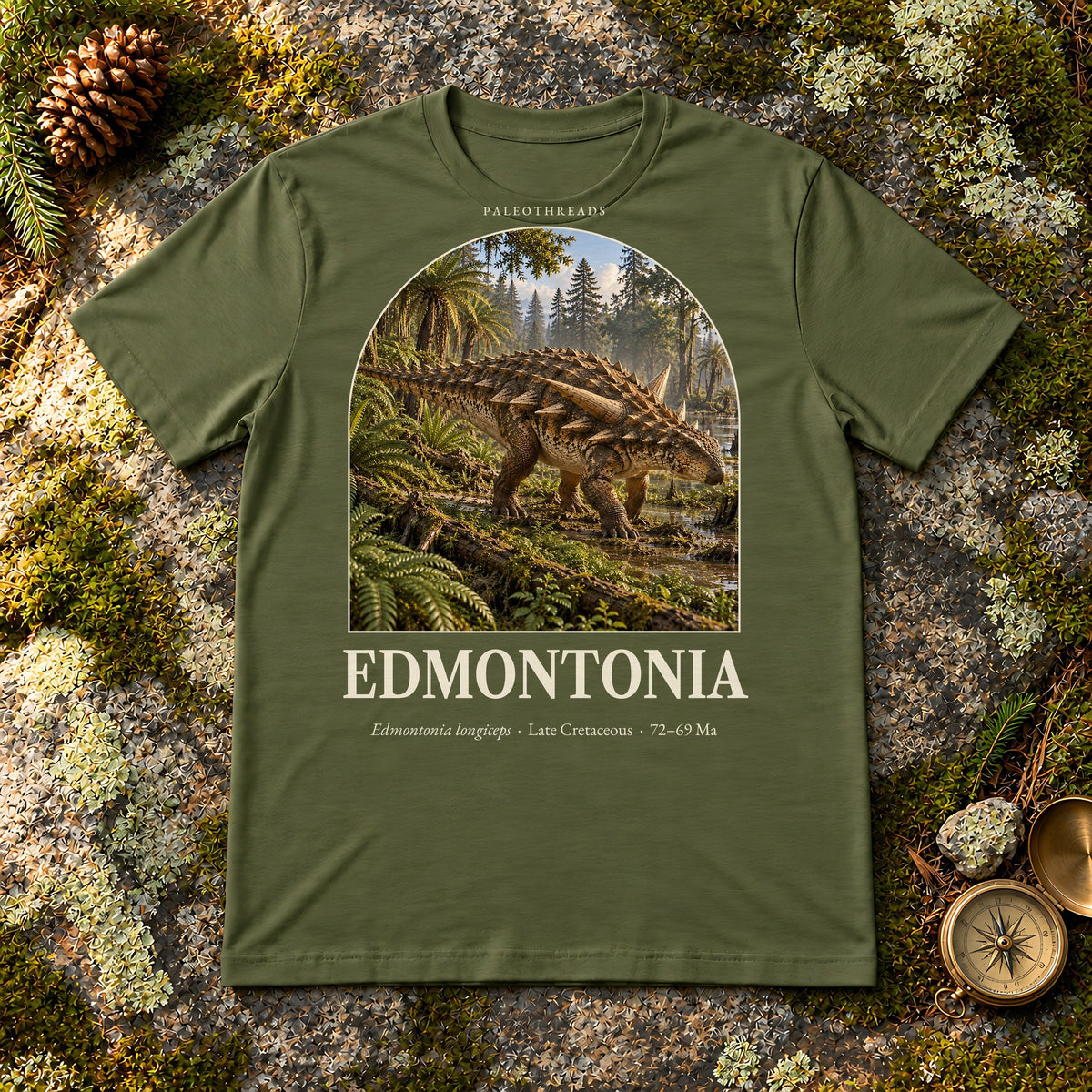 Edmontonia t-shirt flat lay – military green PaleoThreads paleo art tee on mossy rock with a brass compass