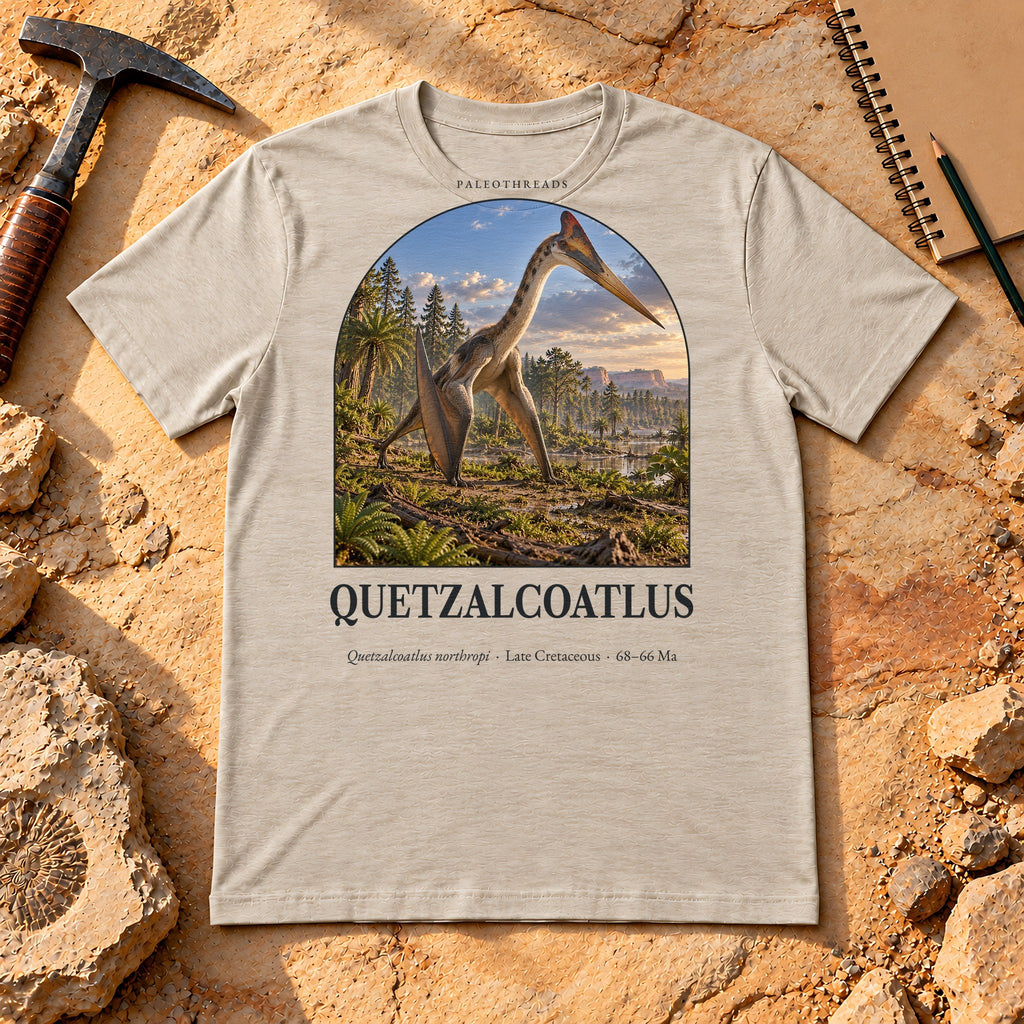 Quetzalcoatlus t-shirt flat lay – heather dust PaleoThreads paleo art tee on sandstone with a rock hammer