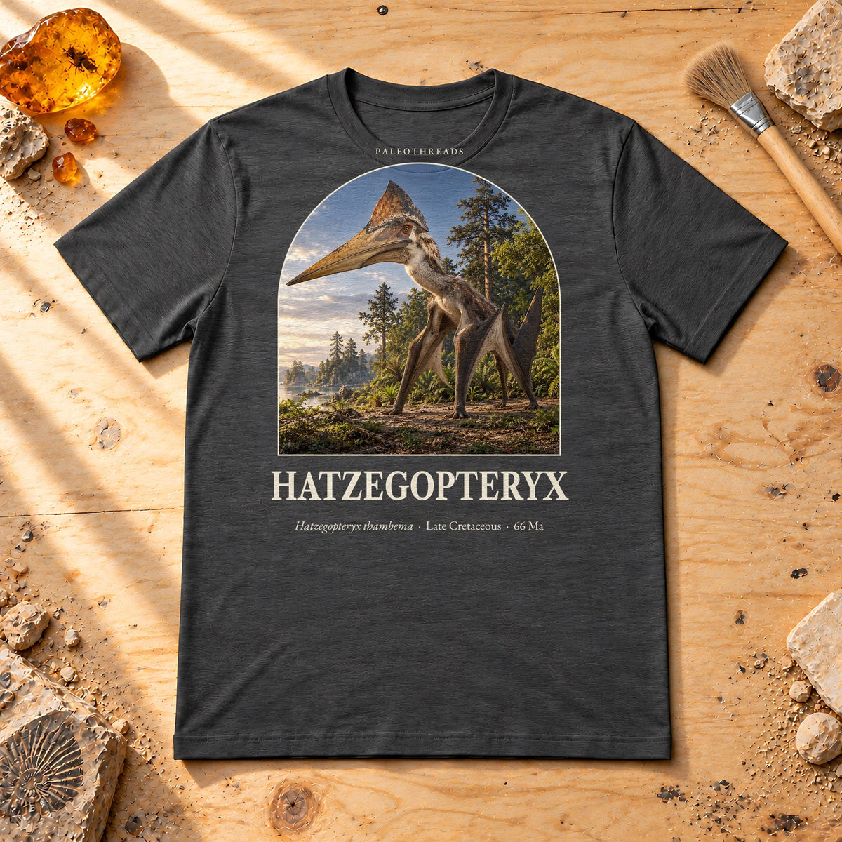 Hatzegopteryx t-shirt flat lay – dark grey heather PaleoThreads paleo art tee on a fossil prep bench with amber