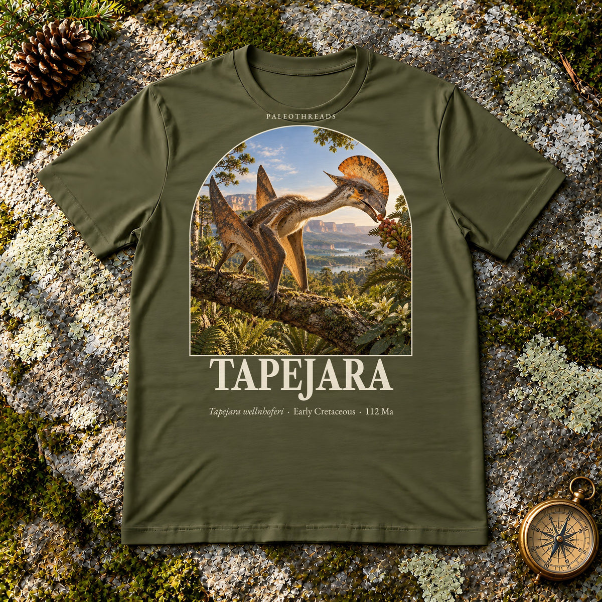 Tapejara t-shirt flat lay – olive PaleoThreads paleo art tee on mossy rock with a brass compass