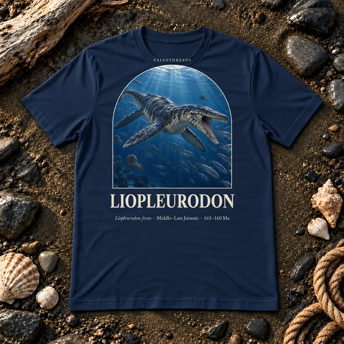 Liopleurodon t-shirt flat lay – navy PaleoThreads paleo art tee on a fossil beach with driftwood