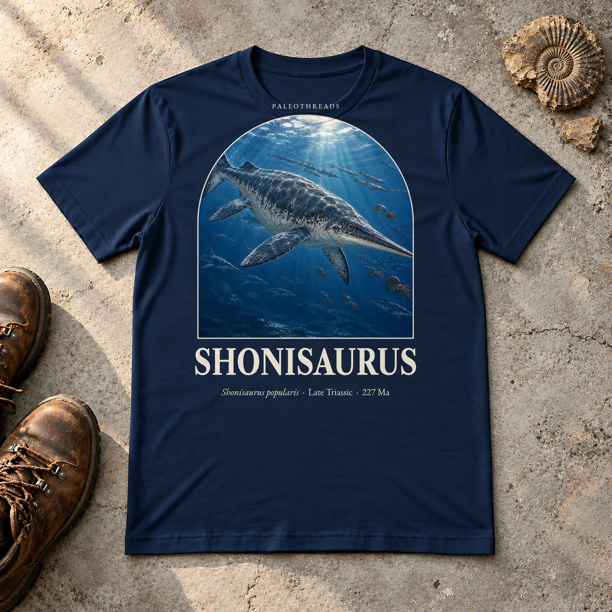 Shonisaurus t-shirt flat lay – navy PaleoThreads paleo art tee with hiking boots and an ammonite