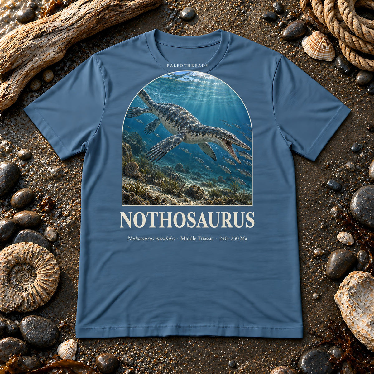Nothosaurus t-shirt flat lay – steel blue PaleoThreads paleo art tee on a fossil beach with driftwood
