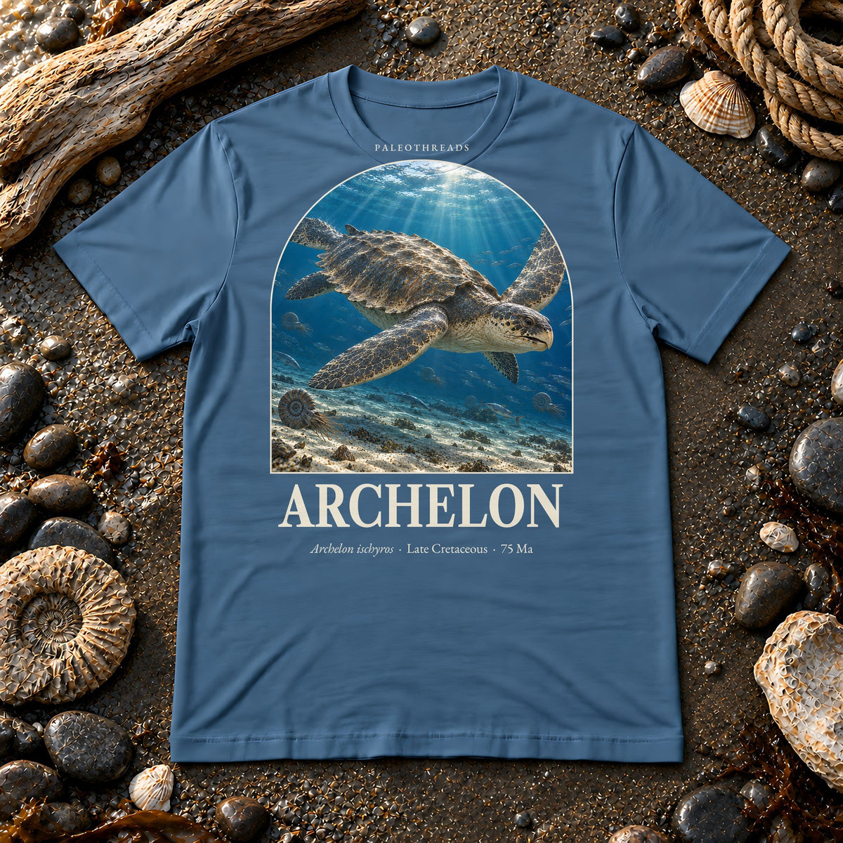 Archelon t-shirt flat lay – steel blue PaleoThreads paleo art tee on a fossil beach with driftwood