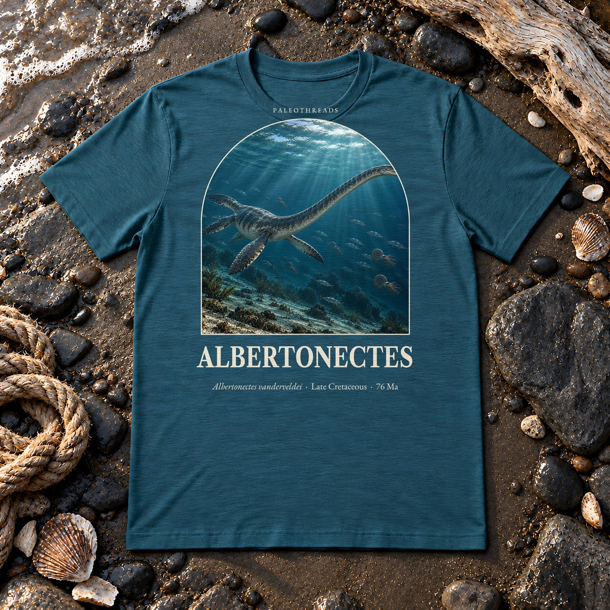 Albertonectes t-shirt flat lay – heather deep teal PaleoThreads paleo art tee on a fossil beach with driftwood