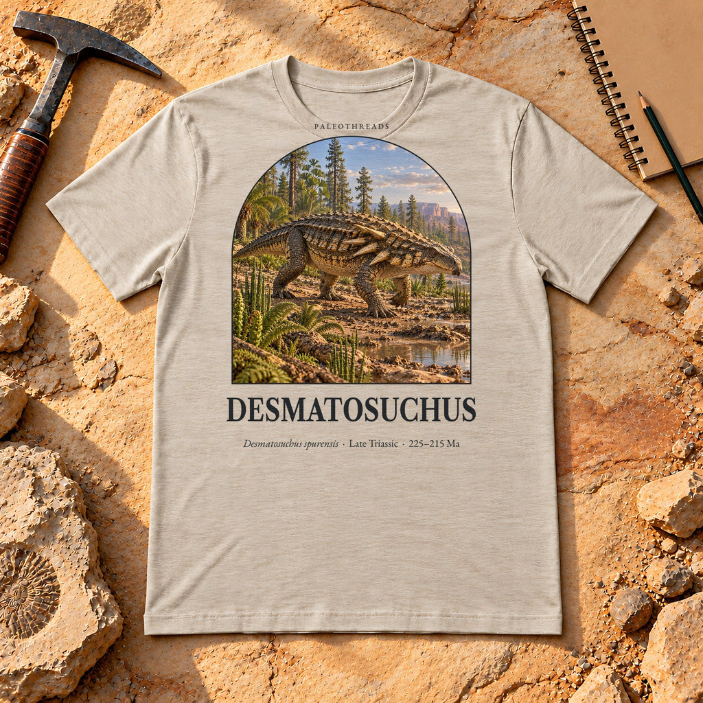 Desmatosuchus t-shirt flat lay – heather dust PaleoThreads paleo art tee on sandstone with a rock hammer