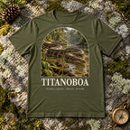 Titanoboa t-shirt flat lay – olive PaleoThreads paleo art tee on mossy rock with a brass compass
