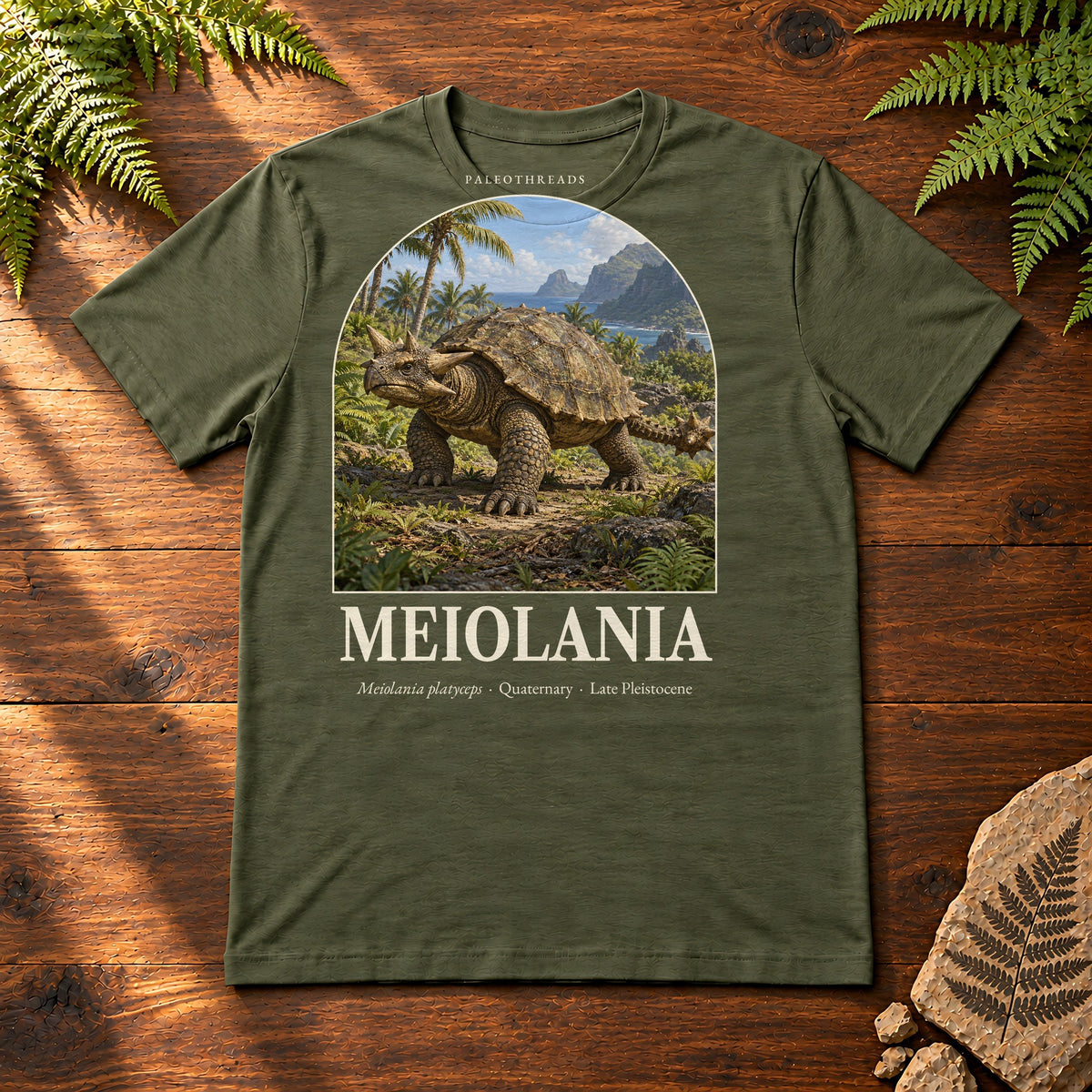 Meiolania t-shirt flat lay – military green PaleoThreads paleo art tee on a walnut field desk with ferns