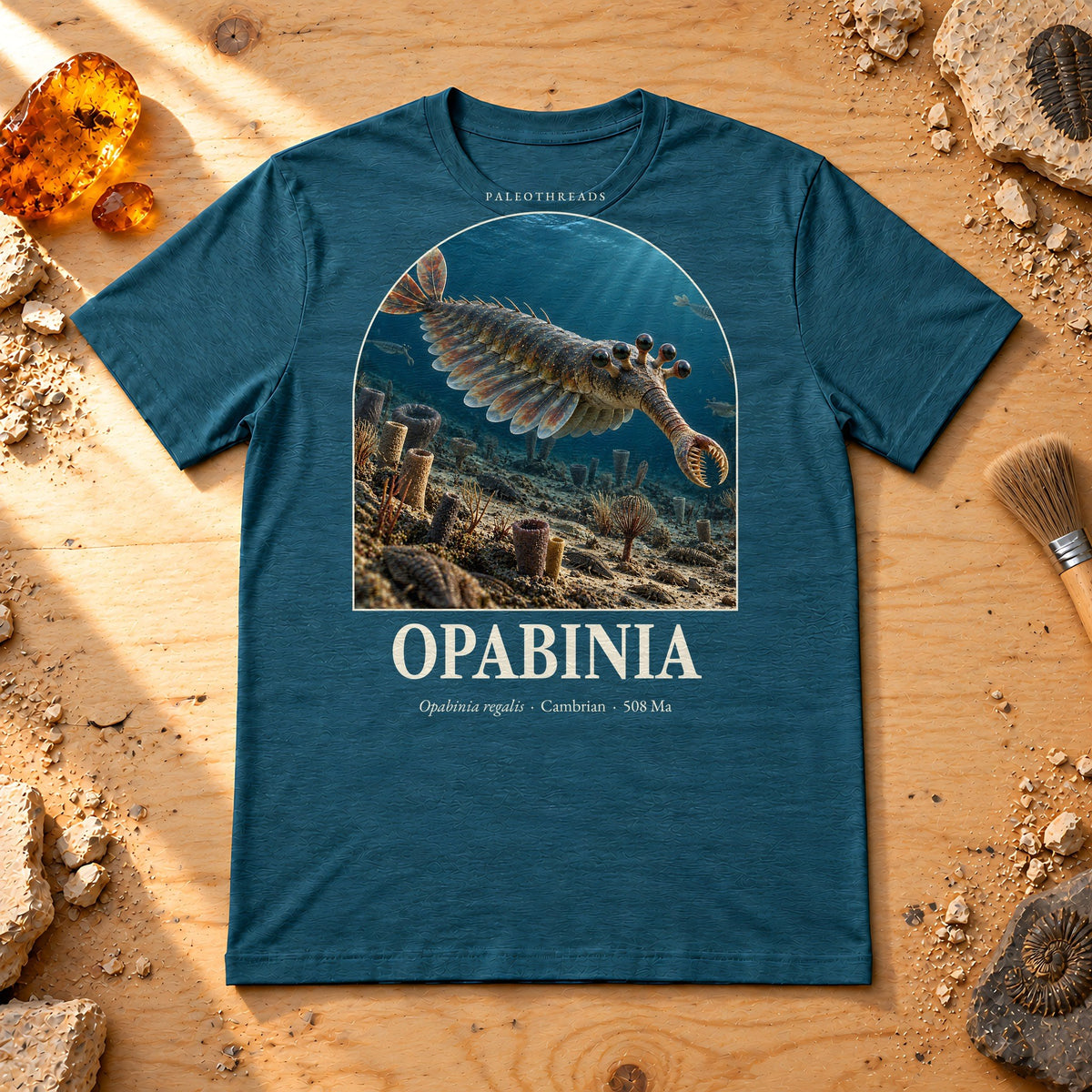 Opabinia t-shirt flat lay – heather deep teal PaleoThreads paleo art tee on a fossil prep bench with amber