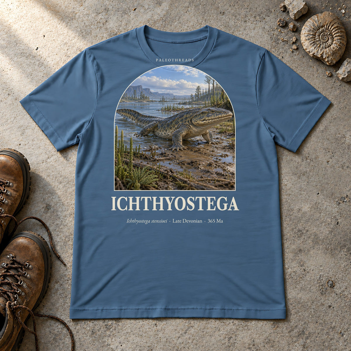 Ichthyostega t-shirt flat lay – steel blue PaleoThreads paleo art tee with hiking boots and an ammonite