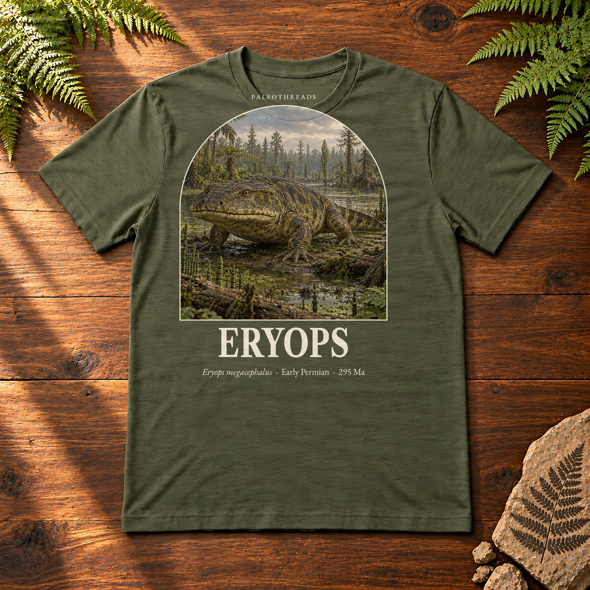 Eryops t-shirt flat lay – military green PaleoThreads paleo art tee on a walnut field desk with ferns