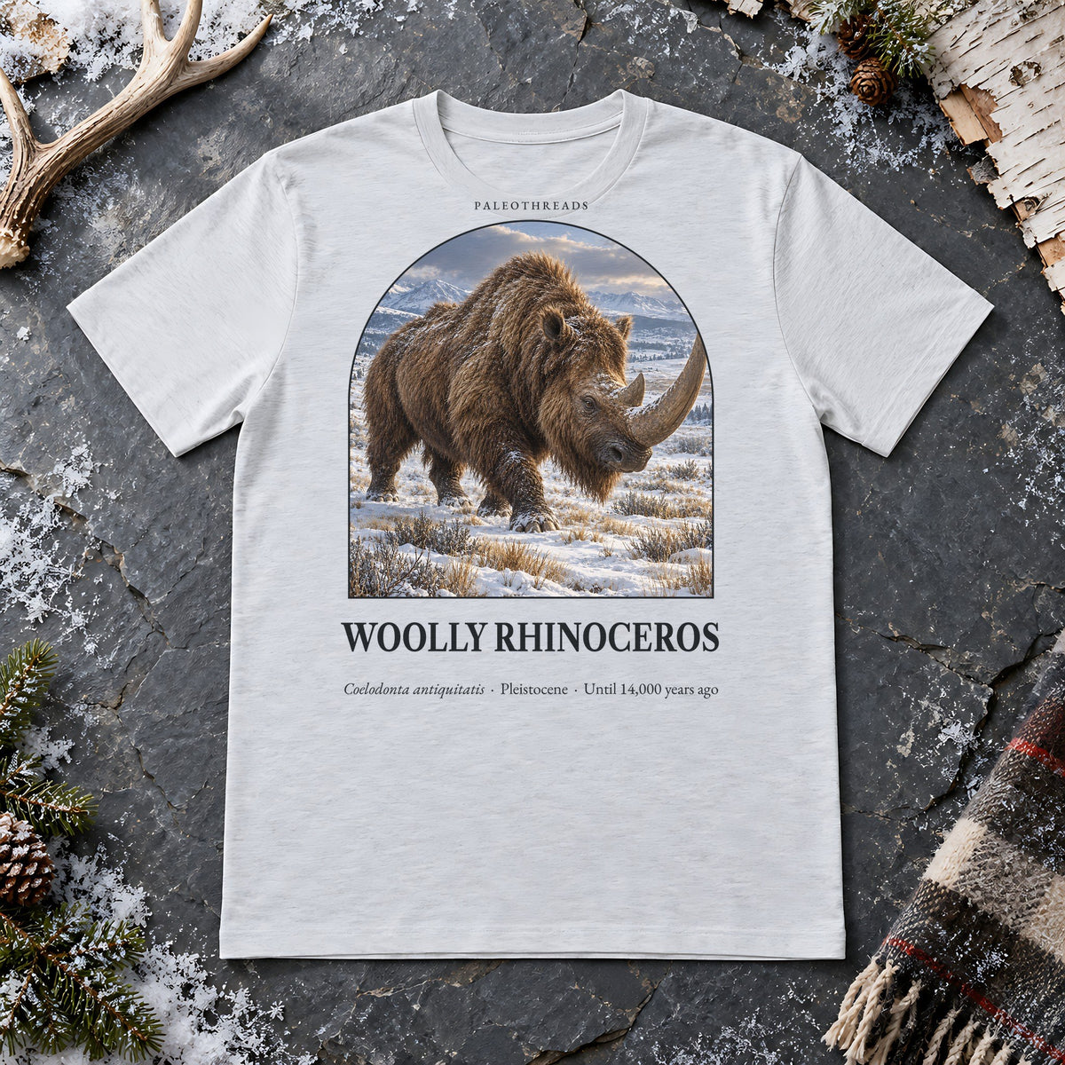 Woolly Rhinoceros t-shirt flat lay – ash PaleoThreads paleo art tee on frosty slate with an antler