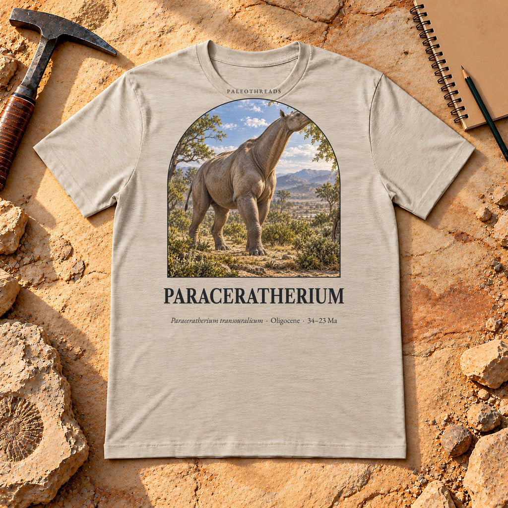 Paraceratherium t-shirt flat lay – heather dust PaleoThreads paleo art tee on sandstone with a rock hammer