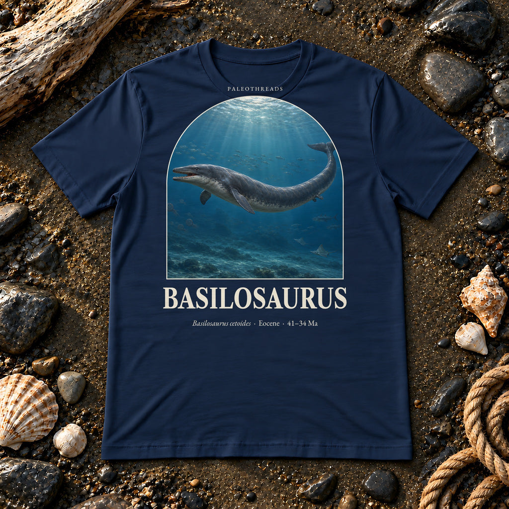 Basilosaurus t-shirt flat lay – navy PaleoThreads paleo art tee on a fossil beach with driftwood