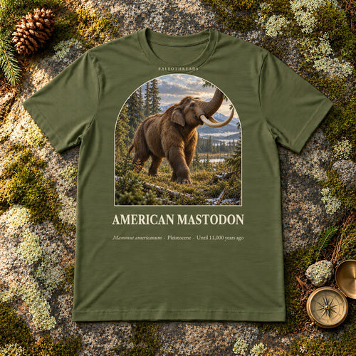 American Mastodon t-shirt flat lay – military green PaleoThreads paleo art tee on mossy rock with a brass compass