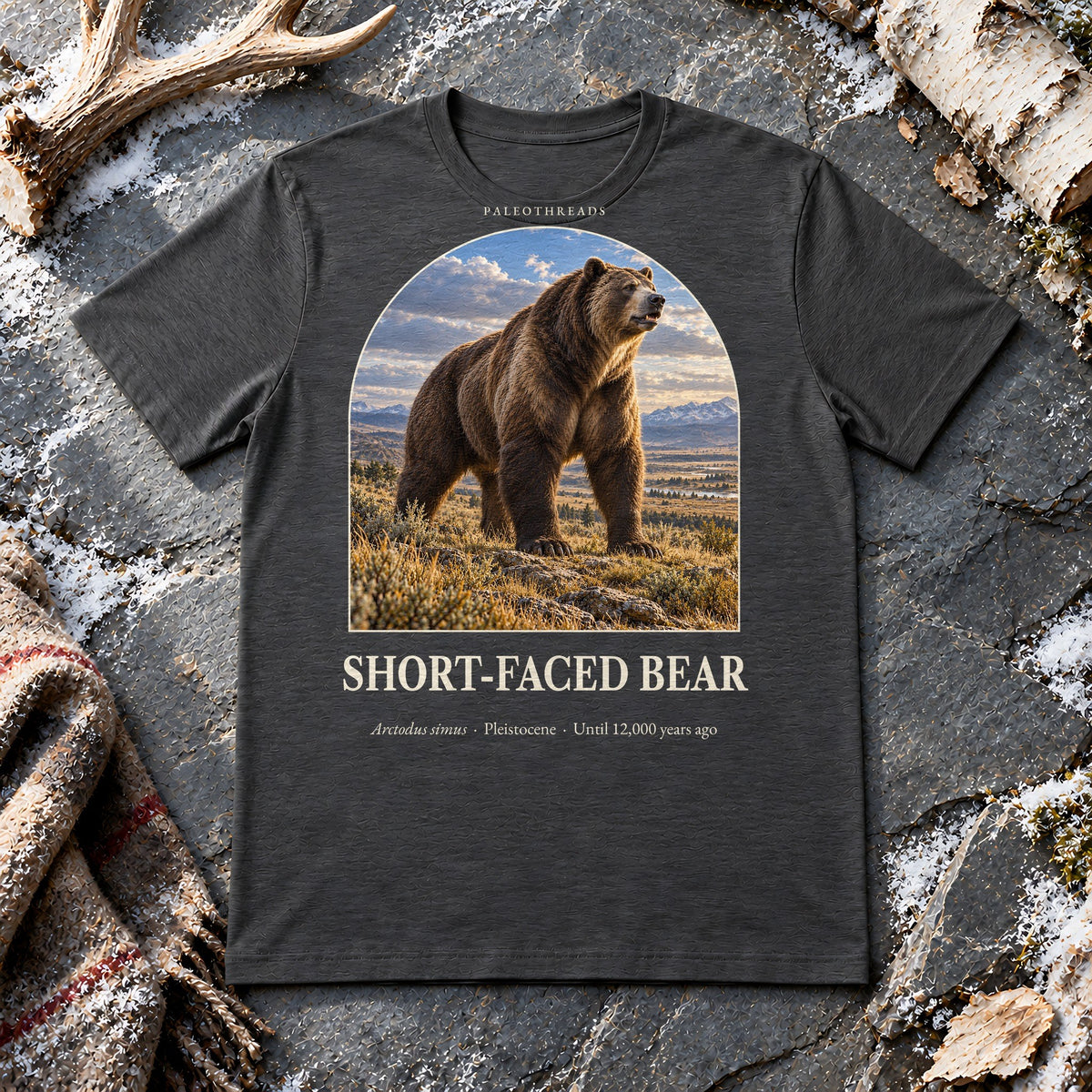 Short-faced Bear t-shirt flat lay – dark grey heather PaleoThreads paleo art tee on frosty slate with an antler