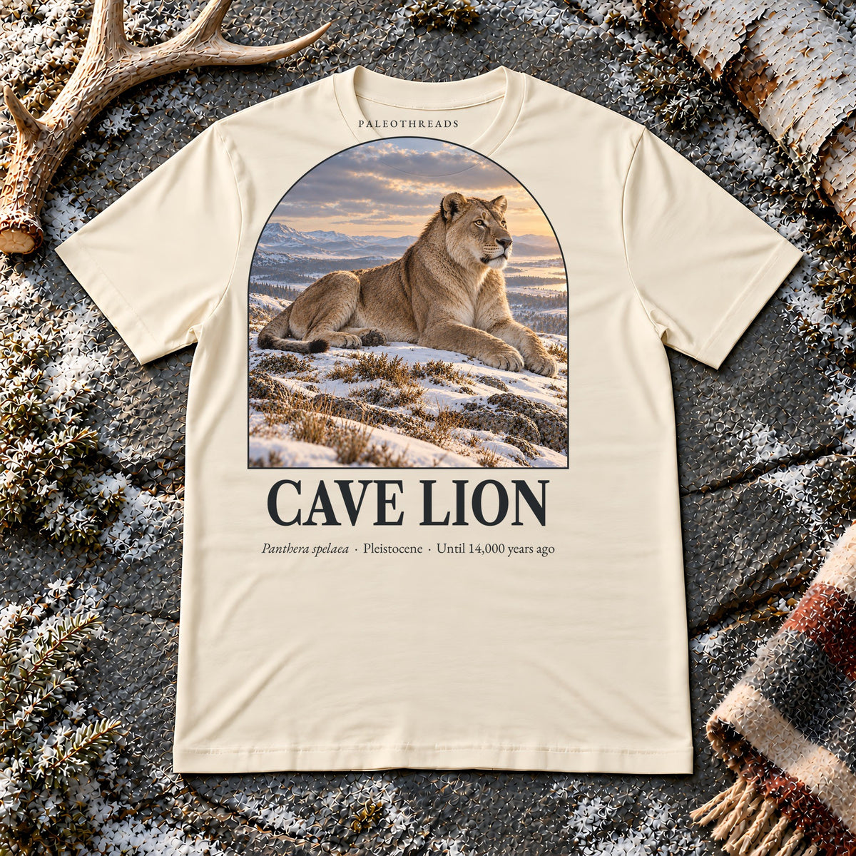 Cave Lion t-shirt flat lay – soft cream PaleoThreads paleo art tee on frosty slate with an antler